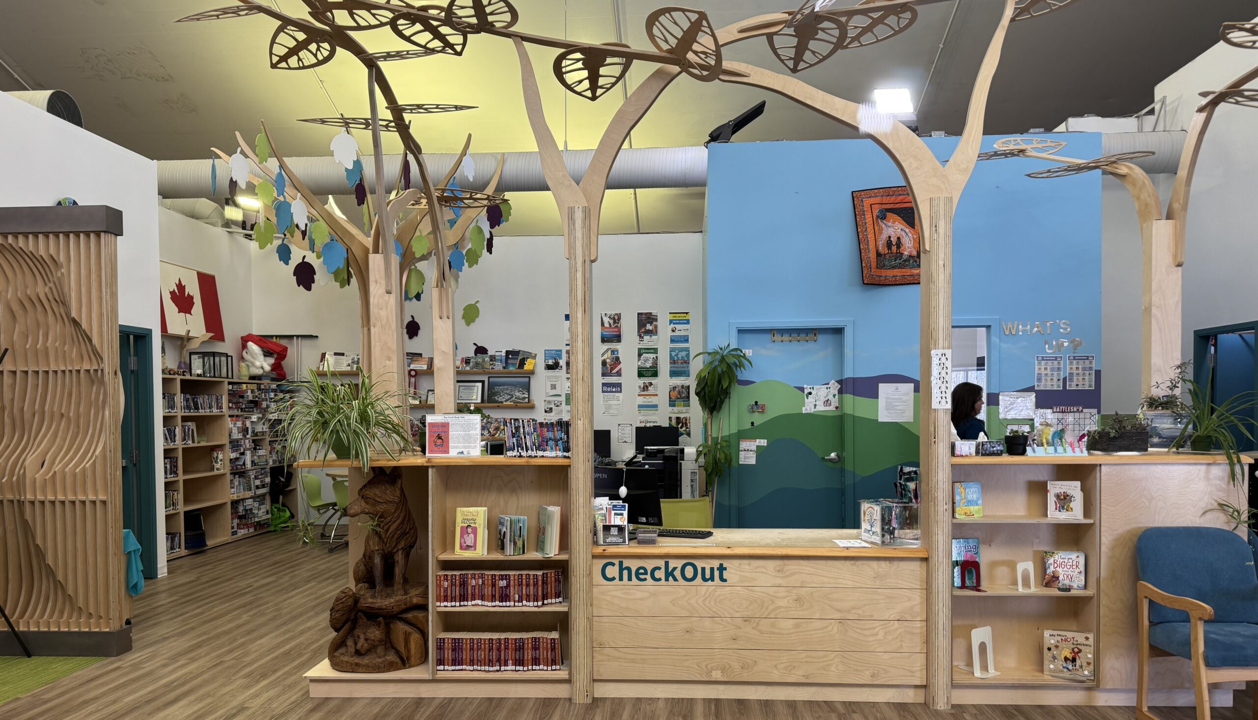Interior shot of the library. The checkout desk has wooden additions coming off it made to look like trees that extend vertically to the roof.